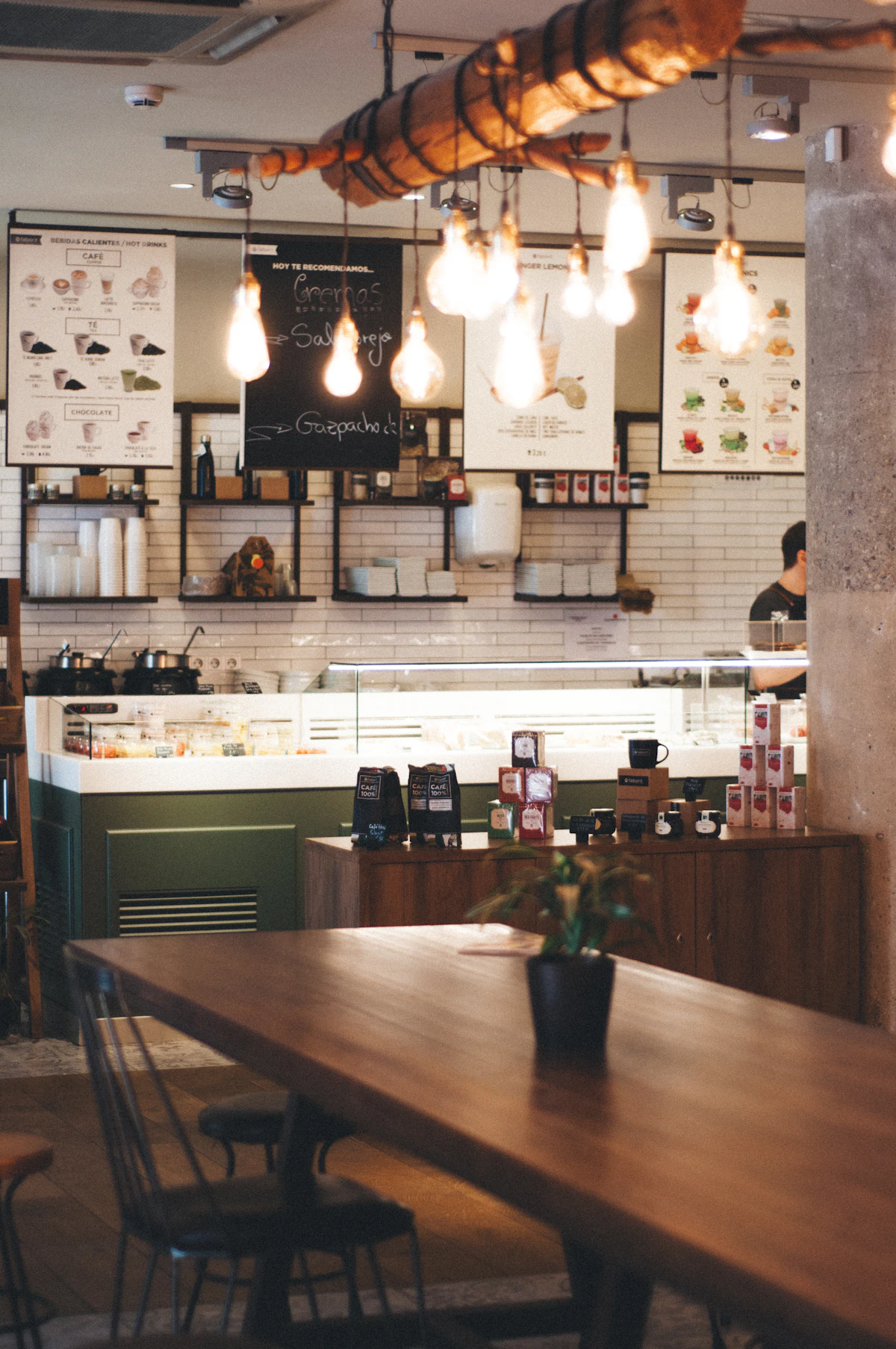 Interior de uma cafeteria com balcão, mesas e luminárias